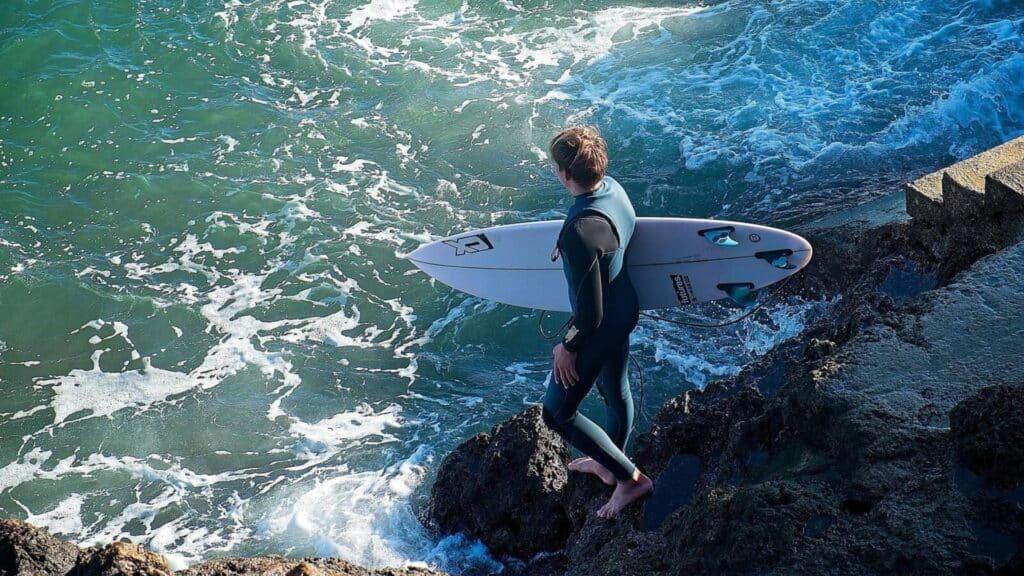 An image of a man holding a surfboard about to enter the sea