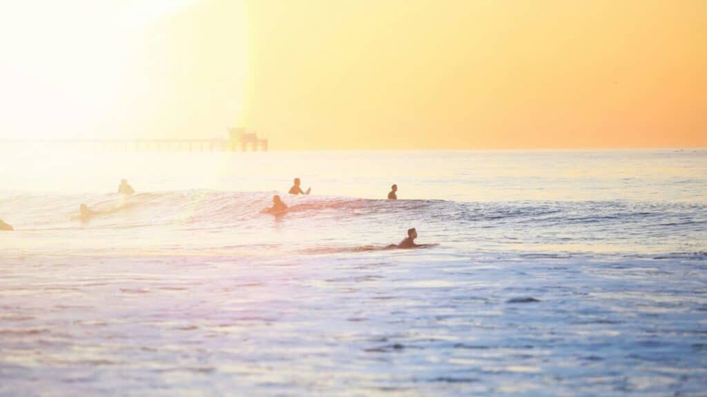 An image of surfers in the sea with the sunset behind 